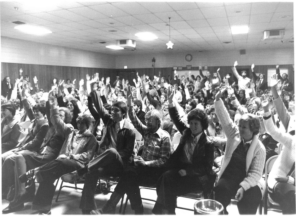 Crowd of people sitting with hands raised.