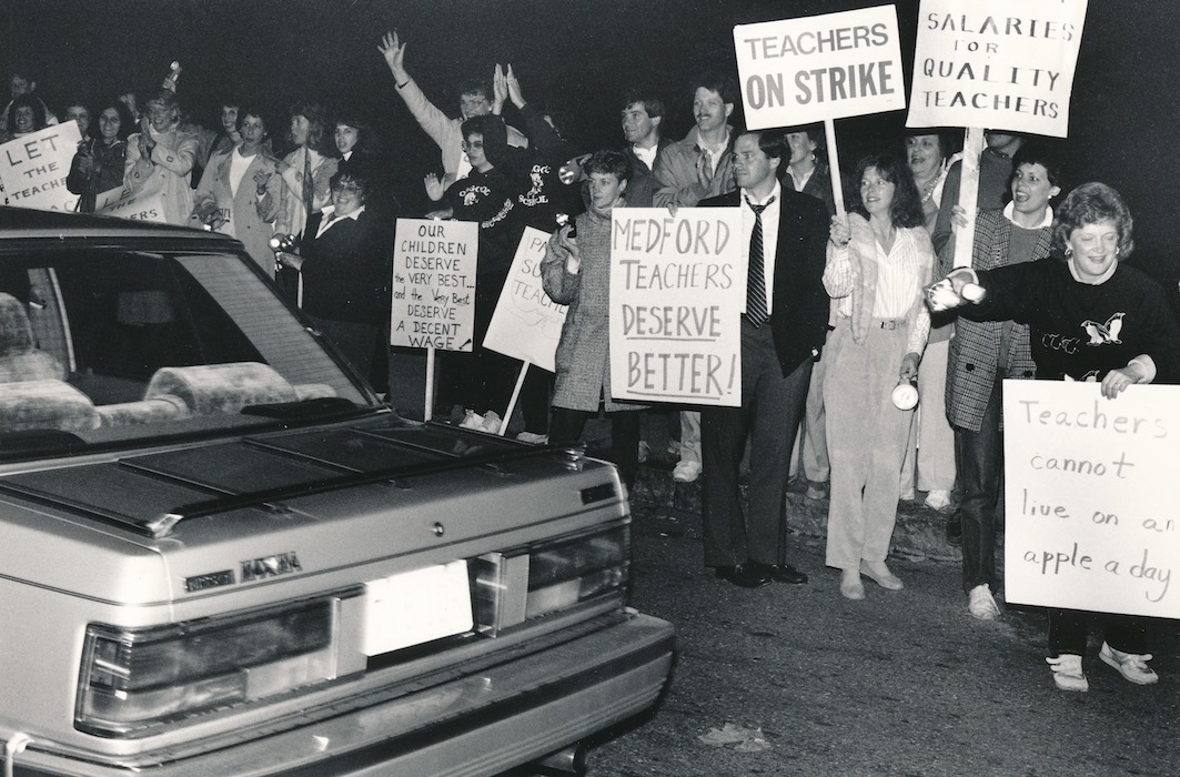 Crowd of picketers with signs waving at a passing car.