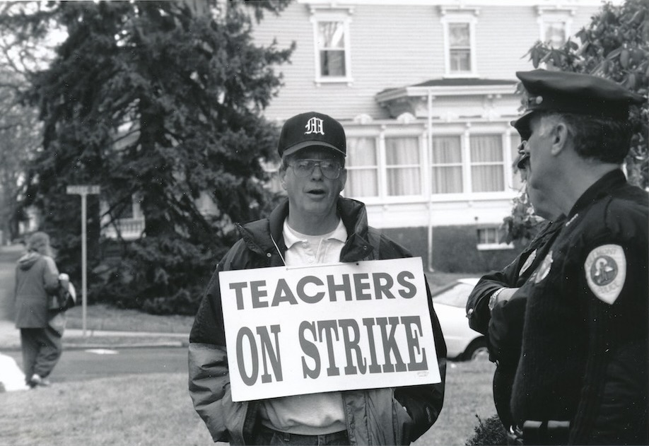 Picketer with sign supporting the Belmont strike standing next to a police officer.