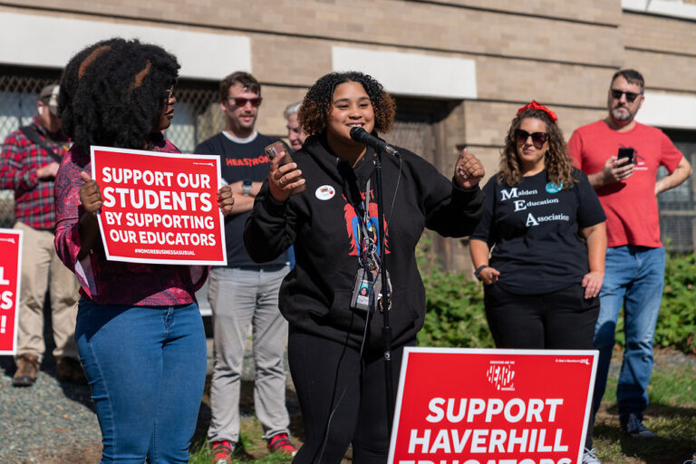 Deja Gutierrez standing in front of a microphone alongside picketers.