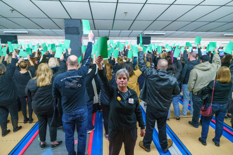 Barbara Locke stands in front of a large crowd that is holding up green papers.