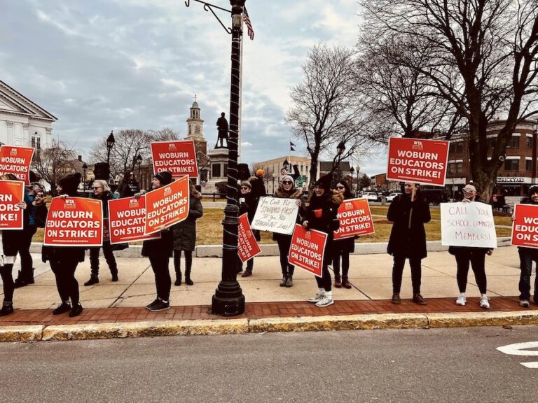 Picketers holding signs supporting the Woburn strike on a sidewalk.