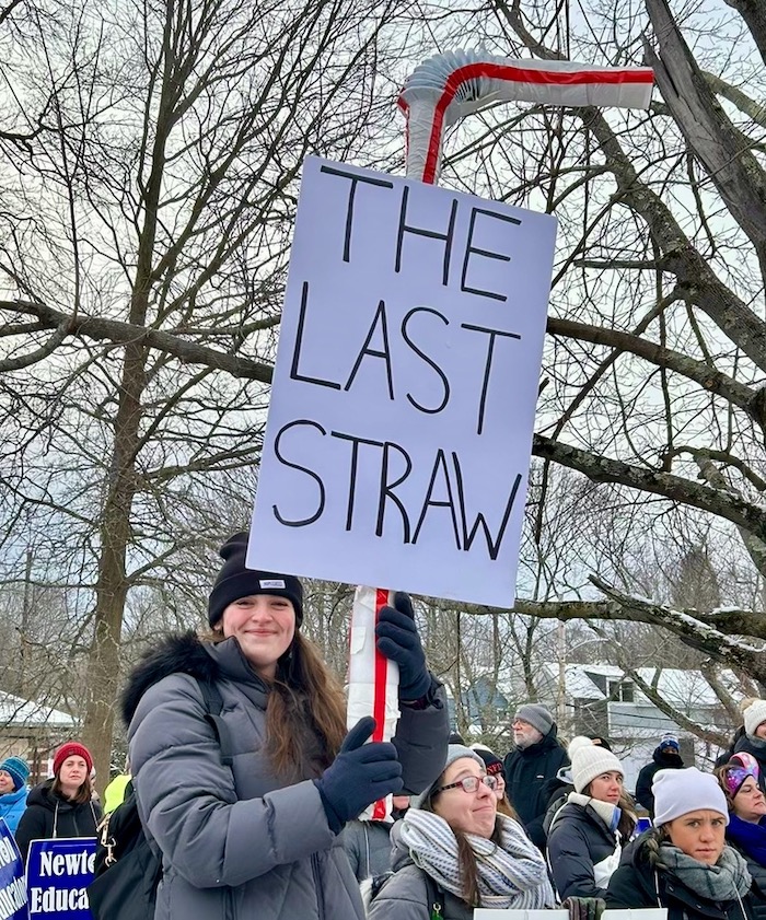 Person with sign shaped like a plastic straw.