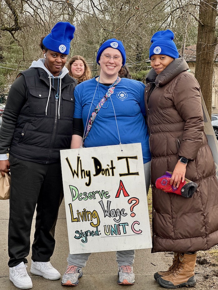 Three people, one holding a sign supporting the Newton strike.