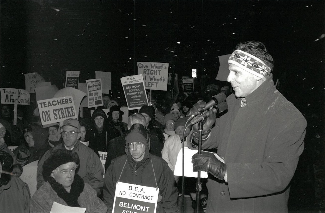 Person in front of a crowd of picketers with a microphone.