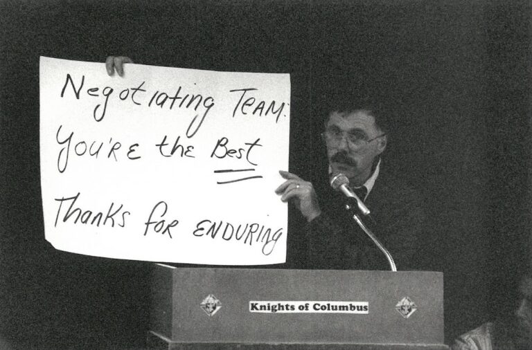 Person with sign supporting the Belmont strike in front of a microphone.