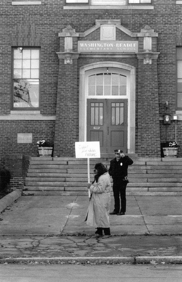 Picketer holding sign supporting the Beverly strike in front of a school and police officer.