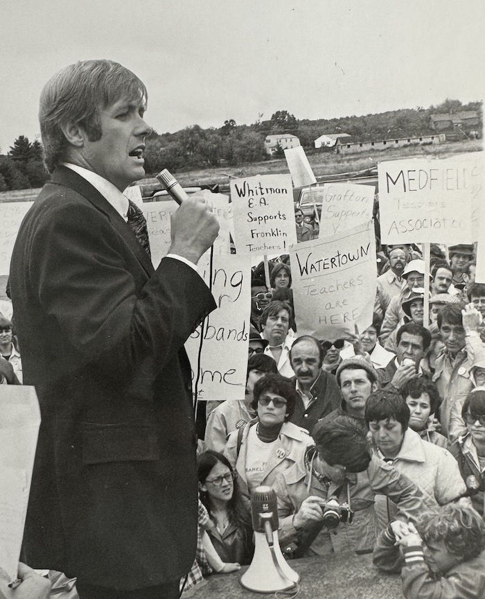 Man with a microphone speaking in front of a crowd holding signs supporting the Franklin strike.