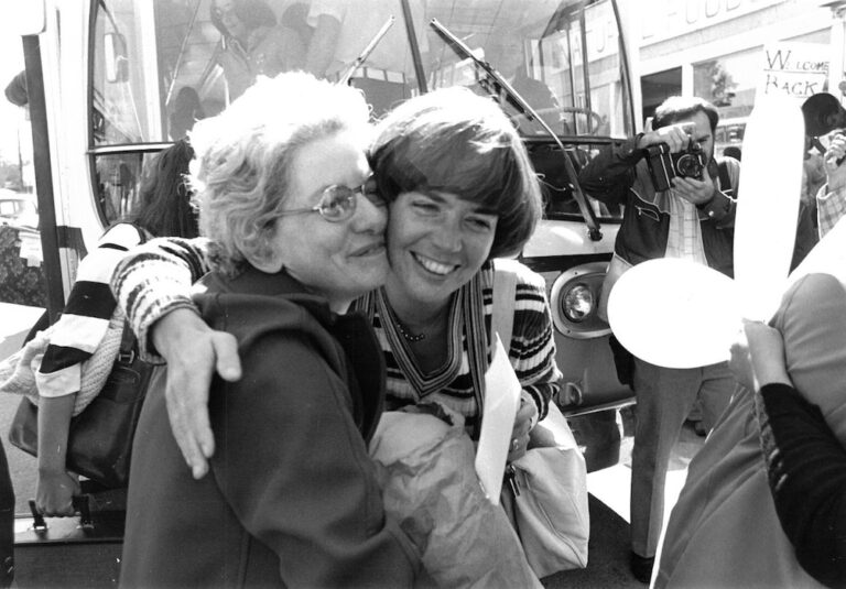 Two people hugging in front of a bus.
