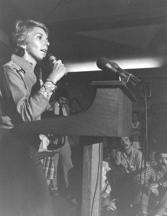 Woman with a microphone speaking in front of a crowd.