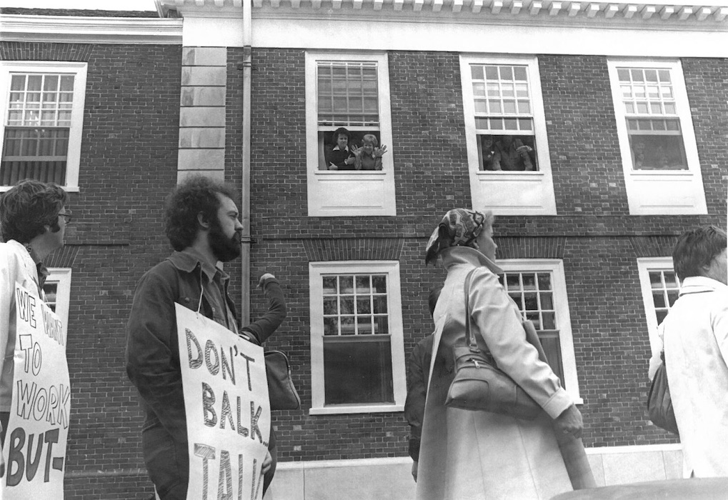 Picket line in front of building with people in the building windows.
