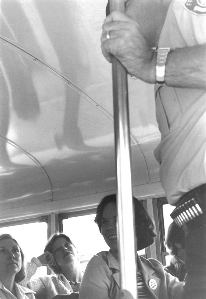 Police officer holding a pole in front of seated people in a bus.