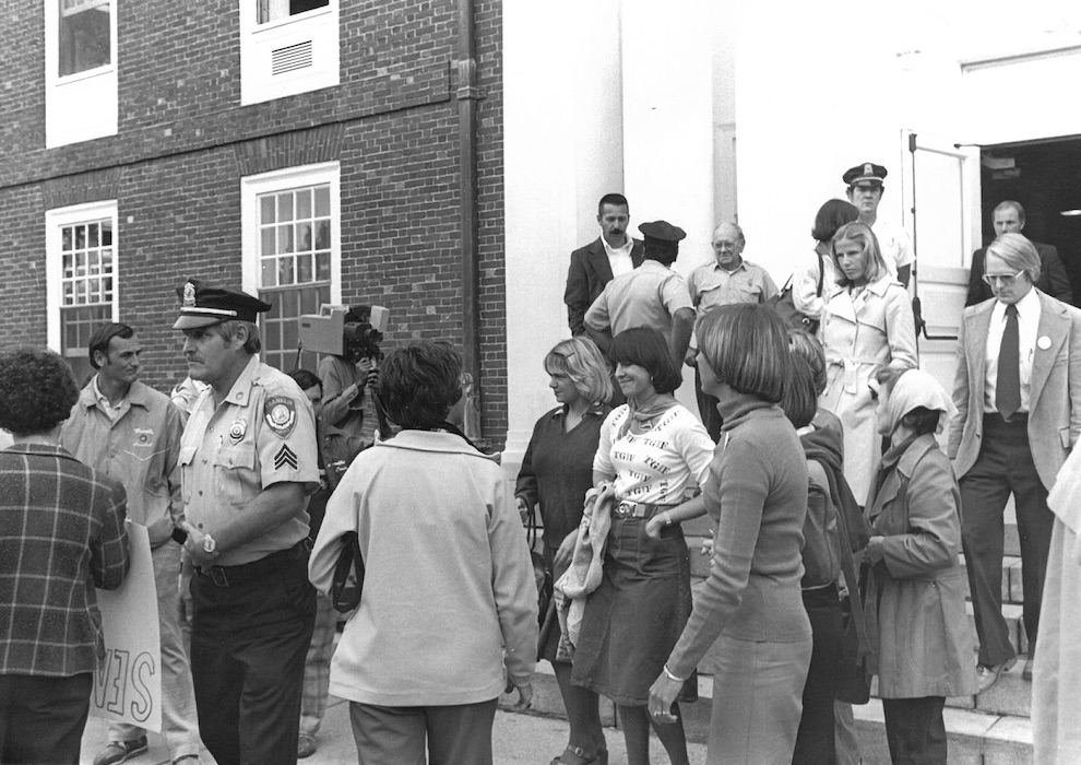 People and police officers gathered in front of building.