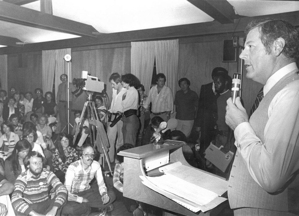 Person with microphone speaking to group of people.