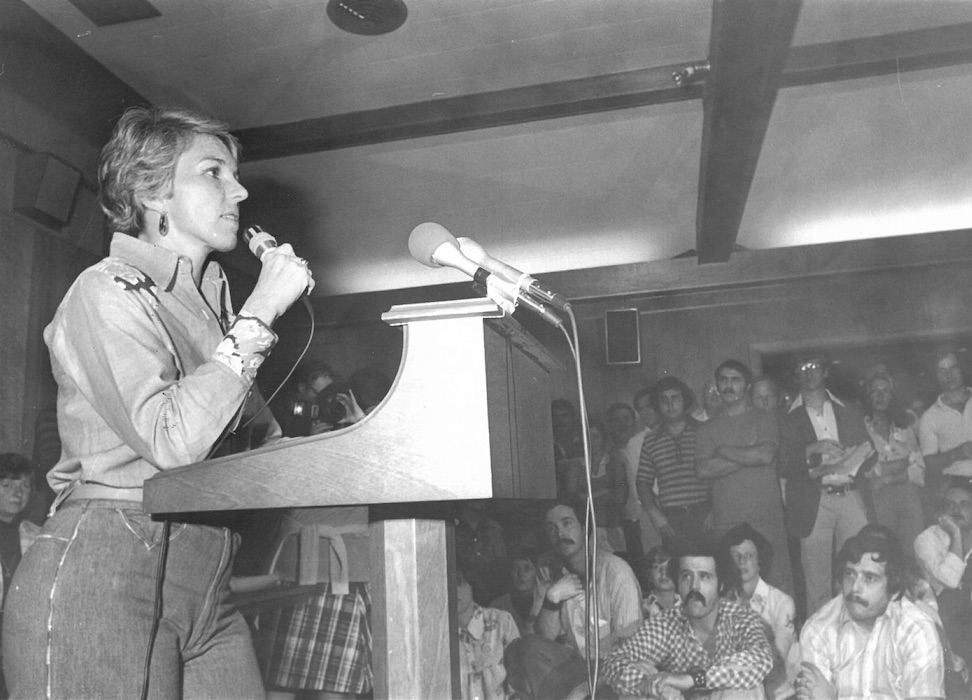 Woman with a microphone speaking to a crowd.