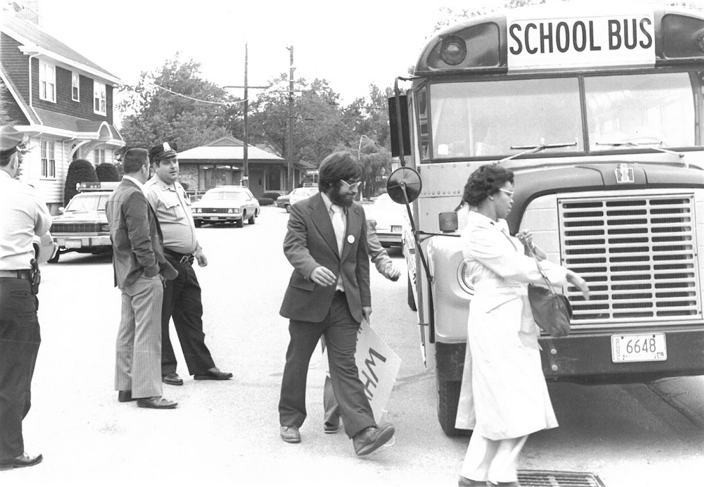 People and police officer in front of a school bus.