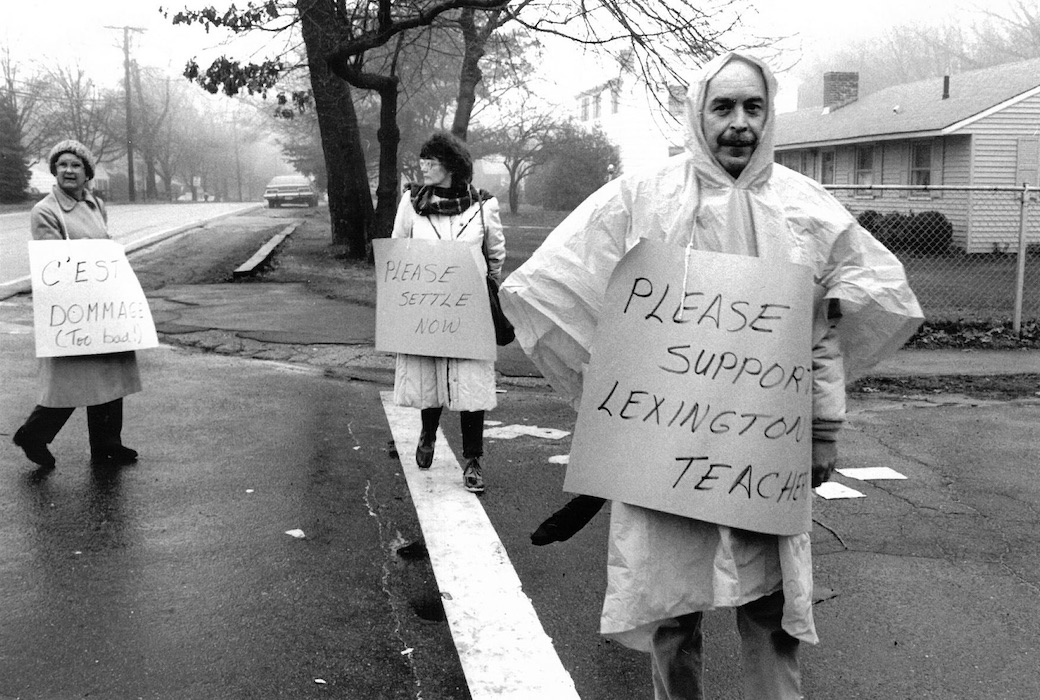 People crossing the street wearing signs supporting the Lexington strike in the rain.