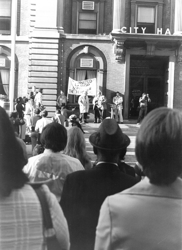 Group of people listening to man behind microphone speak.