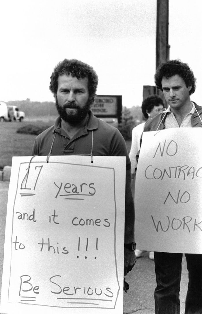 Two picketers on the picket line wearing signs supporting the New Bedford strike.
